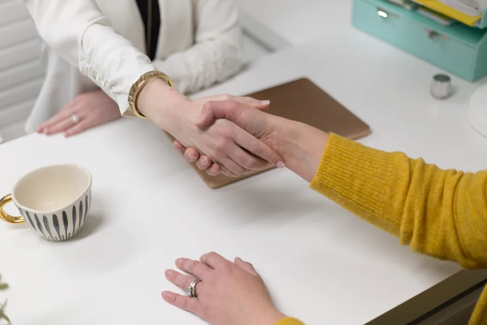 Due persone si stringono la mano su una scrivania, a conclusione di un incontro di lavoro.